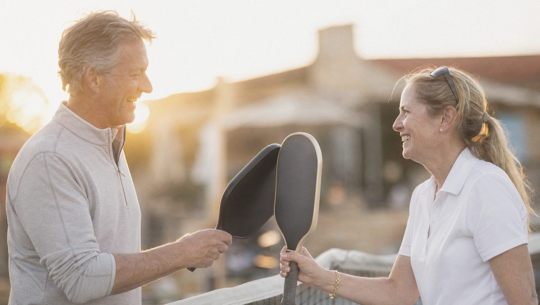 Two members laughing over pickleball paddles